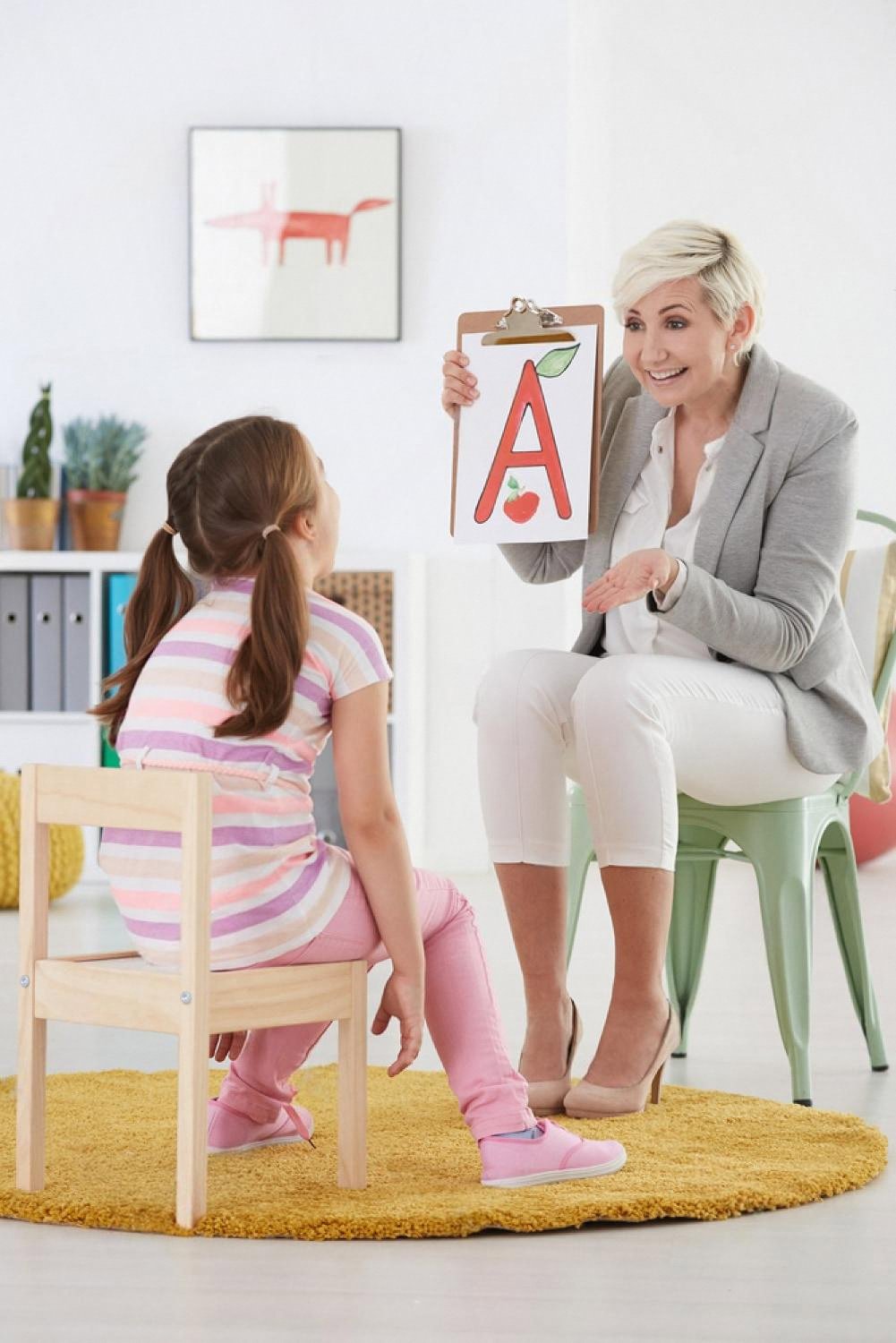 Teacher showing a young girl a flashcard with the letter A during an after-school learning session